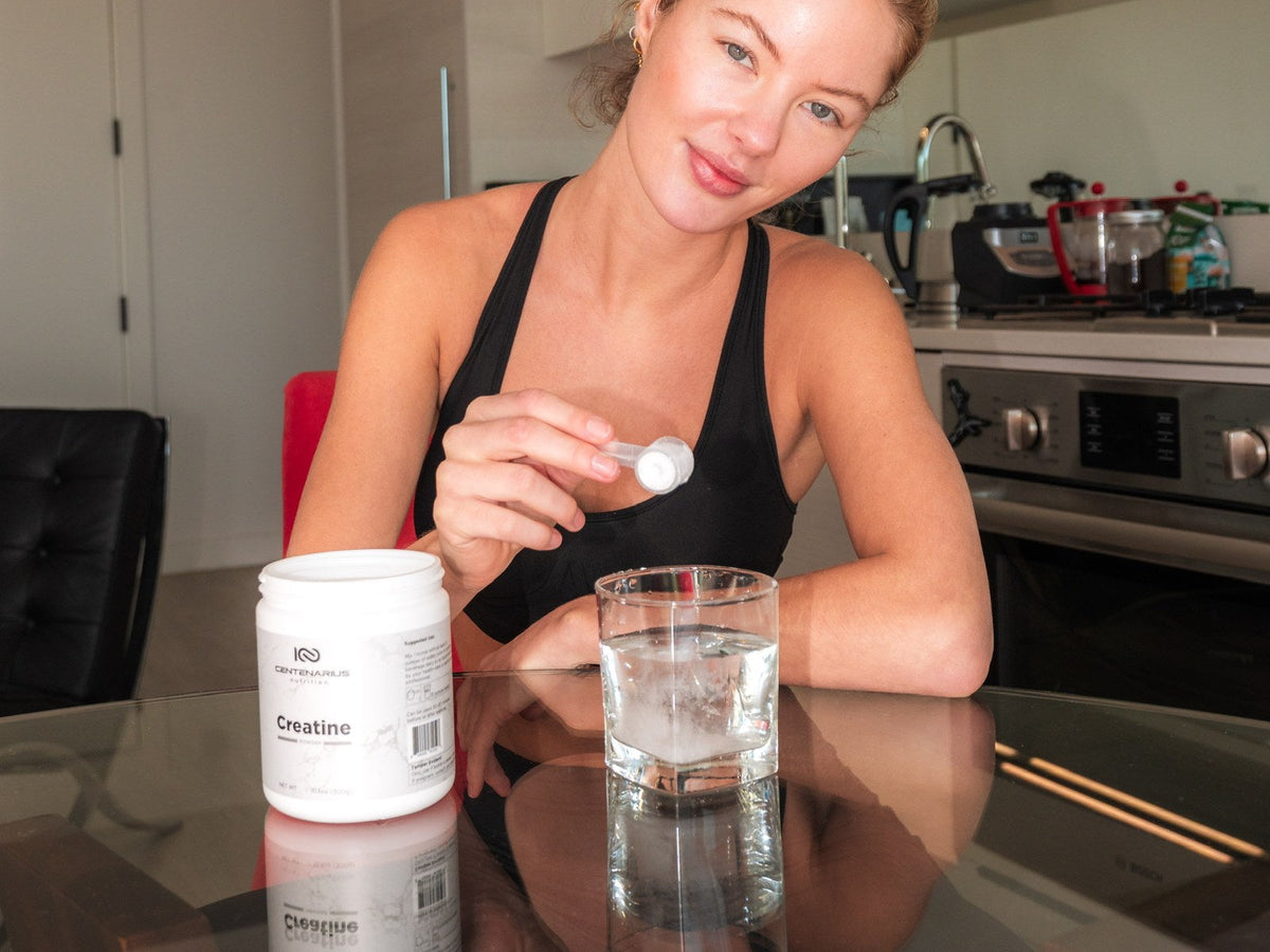 Woman at a kitchen table with a jar of Centenarius creatine and a glass of water